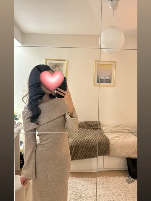 Beige lång stickad klänning - Snygg beige långklänning i stickat material med bred krage som kan bäras offshoulder. Klänningen har lång ärm och figurnära passform, perfekt för en trendig look. Ihopsytt hål längst ner på klänningen.