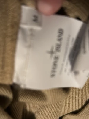 Beige hoodie från Stone Island - Säljer en beige hoodie från Stone Island med den klassiska loggan på vänster ärm. Hoodien har en avslappnad passform och är tillverkad i mjukt bomullsmaterial. Perfekt för dig som gillar streetwear och vill ha något stilrent och bekvämt.
