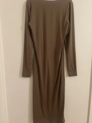 Beige långärmad långklänning - En stilren beige långklänning med lång ärm och rundad urringning. Klänningen har en rak passform och är tillverkad i ett mjukt, stretchigt material som ger en bekväm känsla. Perfekt för dig som gillar minimalistisk och enkel stil.