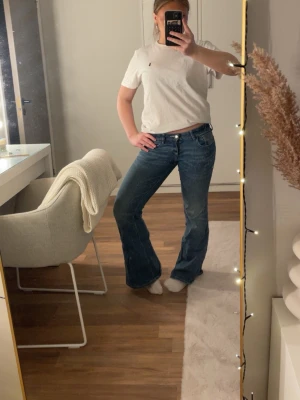 Blå bootcut jeans med låg midja - Säljer ett par klassiska blå bootcut jeans med låg midja och femficksmodell. Jeansen har en snygg tvätt och utsvängda ben som ger en retrovibe. Perfekta till sneakers eller boots och passar dig som gillar en avslappnad men trendig stil.