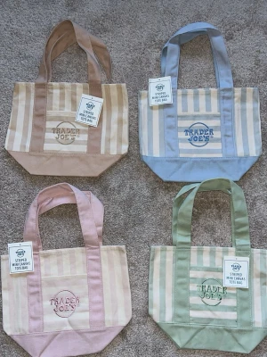Randig shoppingväska Trader Joe's - Säljer en randig minishoppingväska från Trader Joe's i canvas. Finns i flera färger: beige, blå och grön. Väskan har breda axelband, broderad logga på framsidan och praktisk ficka. Perfekt för att bära småsaker eller som accessoar. Denna annons står för väskan i beige.💗