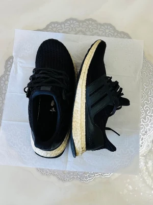 Adidas ultraboost  - Snygga svarta sneakers med stickad ovandel och vit, dämpad sula. Skorna har svarta snören och detaljer i plast på sidorna samt hälpartiet. Perfekta för dig som gillar sportig och modern stil.