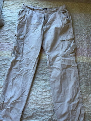 Beige cargobyxor från Saligia XL - Snygga beige cargobyxor från lager 157 i storlek XL. Byxorna har flera praktiska fickor på sidorna och klassisk cargomodell med raka ben. Tillverkade i ett lätt och bekvämt bomullsmaterial, perfekta för en avslappnad stil.