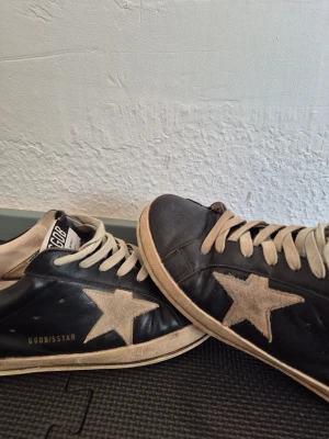 Svarta GGDB sneakers med stjärna - Svarta sneakers från Golden Goose med vit stjärndetalj på sidan och beige snören. Skorna har en klassisk låg profil och vit sula. Materialet är läder och designen har en vintagekänsla med GGDB/SSTAR-tryck på sidan.