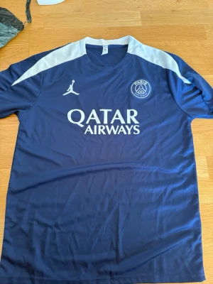 PSG fotbollströja och shorts set - Säljer ett blått PSG matchställ med tröja och shorts. Setet har vita detaljer och logga för Paris Saint-Germain samt Qatar Airways-tryck på bröstet. Tillverkat i lätt och ventilerande material, perfekt för fotbollsträning eller match.