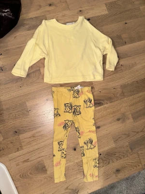 Gult set med tröja och leggings, baby - Sött gult set för baby med långärmad tröja och matchande leggings. Tröjan är enfärgad och leggingsen har tryck med tecknade djur och blad i svart och rosa. Perfekt för lek och mysiga dagar.Gult set med tröja och leggings, baby