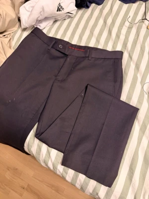 Svarta kostymbyxor Dressmann slim fit - Snygga svarta kostymbyxor från Dressmann i modellen slim fit. Byxorna har klassisk design med pressveck, bälteshällor och knappgylf. Perfekta för dig som vill ha en stilren och modern look. Materialet känns mjukt och följsamt.