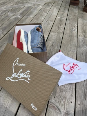 Blåa sneakers från Christian Louboutin - Säljer ett par snygga blåa sneakers från Christian Louboutin i mocka med klassisk röd sula och vita detaljer. Skorna har låga skaft, blåa snören och metallöljetter på sidan. Kommer med originalkartong och dustbag.