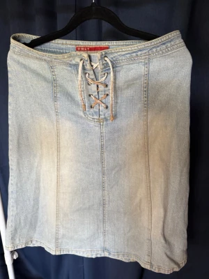 Ljusblå jeanskjol med snörning från ONLY - Ljusblå jeanskjol från ONLY med snygg snörning framtill i midjan. Kjolen har klassisk denimlook och raka sömmar som ger en stilren känsla. Perfekt för dig som gillar en avslappnad och trendig stil.