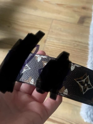 Brunt mönstrat skärp i skinn - Snyggt brunt skärp med klassiskt mönster och detaljer i beige och vitt. Skärpet är gjort i skinn och har en bred design som ger en exklusiv känsla. Perfekt accessoar för att lyfta vilken outfit som helst.