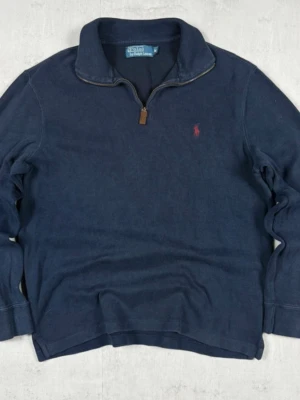 Mörkblå stickad tröja Polo Ralph Lauren - Mörkblå stickad tröja från Polo Ralph Lauren med halv dragkedja och klassisk krage. Tröjan har en liten röd logga broderad på bröstet och ribbade muddar vid ärmslut och nederkant. Perfekt för lager på lager och en avslappnad stil. Den är replika.