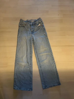 Ljusblå raka jeans - Säljer ett par ljusblå jeans med rak passform och klassisk femficksdesign. Jeansen har normal midja och är tillverkade i denim. Perfekta för en avslappnad och trendig stil. storlek 150
