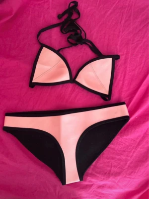 Ljusrosa bikini från Triangl - Supersnygg ljusrosa bikini från Triangl med svarta kanter. Klassisk trekantsmodell upptill och matchande trosor. Materialet är tjockare och känns lyxigt, perfekt för strandhäng eller poolparty. Använd enstaka gång!