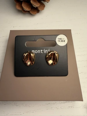 Guldiga örhängen från Montini - Säljer ett par guldiga örhängen från Montini med en cool, organisk och skulptural form. De har en blank finish och är perfekta för dig som gillar statement-accessoarer. Materialet ser ut att vara metall med guldfärgad yta.