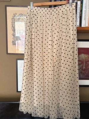 Ny, H&M Beige långkjol med svarta prickar, st M - Säljer en beige långkjol med svarta prickar och elastisk midja. Kjolen har ett luftigt och flowy tyg som ger en snygg siluett. Perfekt för dig som gillar en lekfull och trendig stil.