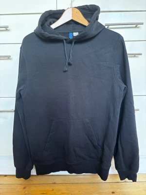 Svart oversized hoodie med ficka och huva från Dividef storlek XS - En klassisk svart hoodie med stor känguruficka framtill och justerbar huva med dragsko. Hoodien har ribbade muddar vid ärmslut och nederkant. Oversized storlek XS