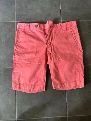Rosa shorts i bomull - Säljer ett par snygga rosa shorts i bomull med normal passform. Shortsen har bälteshällor, knapp och dragkedja framtill samt fickor både fram och bak. Perfekta för varma dagar och enkel att matcha med olika stilar.