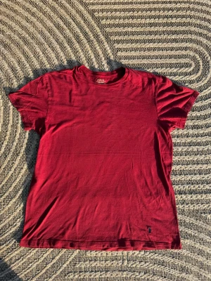 Röd t-shirt Ralph Lauren 100% bomull - Snygg röd t-shirt i bomull med klassisk passform och korta ärmar. En liten broderad detalj syns längst ner på framsidan. Perfekt för en avslappnad och stilren look.