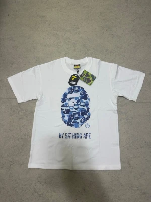 Vit BAPE t-shirt med blått camomönster - Snygg blå Bape tröja med hög kvalitet och bekväm passform. Tröjan är helt ny och oanvänd, perfekt för vardag eller streetwear-stil.  Information: * Märke: Bape * Färg: Blå * Storlek: S * Helt ny och oanvänd * Skön att ha på sig * Hög kvalitet  Skickas eller hämtas enligt överenskommelse. Hör gärna av dig vid frågor eller intresse!