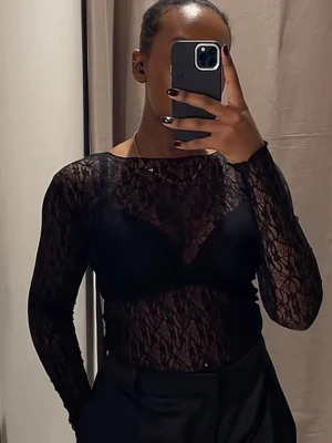 Spetstopp Zara - Säljer en svart, transparent spetsblus med lång ärm och rund hals. Blusen har ett elegant spetsmönster och sitter tight mot kroppen. Perfekt för dig som vill ha en edgy och trendig look.