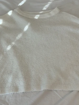 Vit stickad tröja från 157 - Mysig vit stickad tröja från 157 med rund halsringning och ribbade muddar vid hals och nederkant. Perfekt för lager på lager och enkel att matcha med olika outfits. Materialet känns mjukt och bekvämt.
