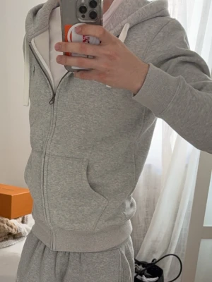 Grå zip hoodie från Polo Ralph Lauren - Säljer en ljusgrå hoodie med dragkedja från Polo Ralph Lauren. Hoodien har vit dragsko, två fickor framtill och den klassiska blå loggan broderad på bröstet. Tillverkad i mjukt sweatshirtmaterial och har ribbade muddar vid ärmar och midja.