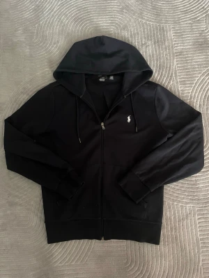 Äkta Ralph Lauren Hoodie - Säljer en äkta, marin blå Ralph Lauren hoodie/zip-up som är köpt på Zalando och i nypris går för 2395kr. Den tagits väl hand om och det finns inte en ända defekt någonstans under den 2 åren jag haft den. Riktigt najs tröja om jag får säga det själv men har haft den så länge och börjar tröttna lite på den och därför säljs den. Skriv om ni har några funderingar. Tack i förväg!