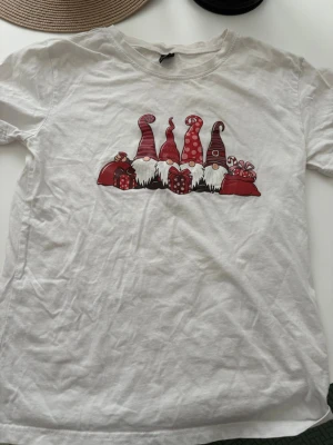 Vit t-shirt med tomtar  - Vit t-shirt i bomull med tryck av fyra söta tomtar i röda luvor och flera julklappar framtill. Oanvänd i storlek S😊