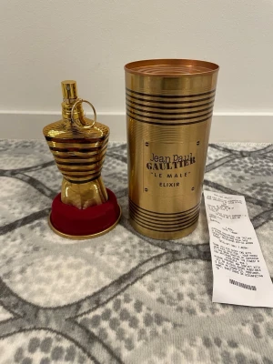 Jean Paul Gaultier Le Male Elixir - Exklusiv parfym från Jean Paul Gaultier, Le Male Elixir. Flaskan är formad som en torso och har en glänsande guldfinish med svarta ränder. Levereras i en matchande guldfärgad metallburk med röda detaljer. Perfekt för dig som vill ha något unikt och lyxigt.