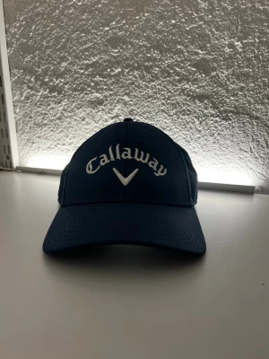 Mörkblå Callaway keps - Snygg mörkblå keps från Callaway med böjd skärm och broderad vit logga framtill i nyskick. Perfekt för golf. Säljs då den inte kommer till användning numera. Skicka vid frågor och/eller funderingar✨