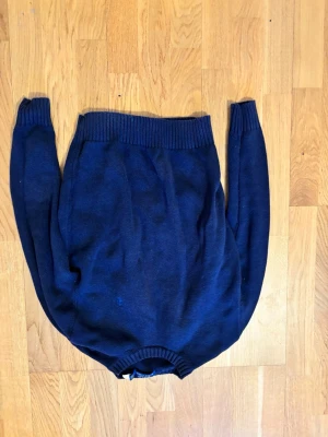 Mörkblå stickad tröja - Mörkblå stickad tröja med rund halsringning och ribbade muddar vid ärmslut och nederkant. Klassisk och enkel design som passar till det mesta. Perfekt för kyligare dagar.