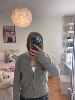 Grå kofta med pärlknappar - Mysig grå kofta med rund hals och pärlknappar framtill. Koftan har långa ärmar och är stickad i ett mjukt material som passar perfekt till jeans. Enkel och stilren design som är lätt att matcha.