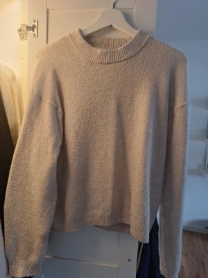 Beige stickad tröja från H&M - Mysig beige stickad tröja från H&M med avslappnad passform och ribbad rund halsringning. Tröjan har långa ärmar och ribbade muddar vid ärmslut och nederkant. Perfekt för lager på lager under kyliga dagar.