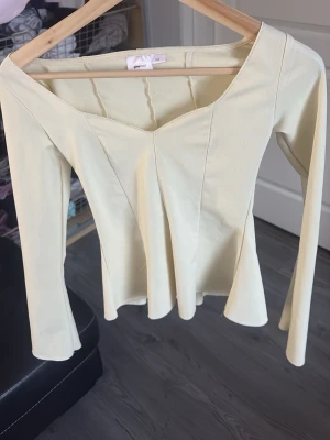 Ljusgul långärmad topp från Gina Tricot - Trendig ljusgul topp från Gina Tricot med lång ärm och snygg v-ringad halsringning. Figurnära passform med sömdetaljer framtill som ger en smickrande siluett. Perfekt att styla med jeans eller kjol för en fräsch look.