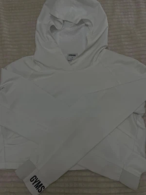 Vit hoodie från Gymshark - Säljer en stilren vit hoodie från Gymshark i storlek S. Hoodien har en klassisk huva och ribbade muddar med Gymshark-logga på ärmen. Använd endast en gång, för liten för mig… 
