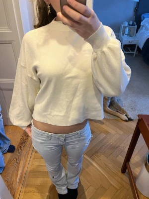 Vit croppad stickad tröja - Säljer en vit croppad stickad tröja. Tröjan har en avslappnad passform och hög hals, perfekt för en trendig och enkel look. Materialet känns mjukt och bekvämt mot huden.