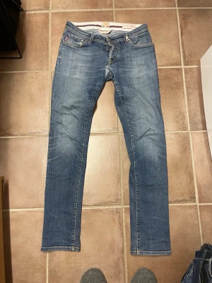 Blå jeans från Tramarossa - Snygga blå jeans från Tramarossa med klassisk femficksdesign och raka ben. Jeansen har diskreta slitningar och kontrastsömmar, samt detaljer som broderad logga och knappgylf. Tillverkade i Italien, detaljer samt material av högsta kvalitet.