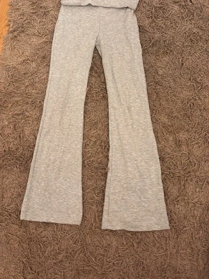 Gråa utsvängda mjukisbyxor - Säljer ett par ljusgrå mjukisbyxor med utsvängda ben. Byxorna har en enkel och clean look utan synliga loggor eller detaljer. Perfekta för en chill och avslappnad stil. Materialet känns mjukt och stretchigt, vilket gör dem riktigt bekväma att ha på sig.