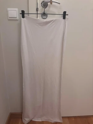 Vit långkjol  - Säljer en enkel och stilren vit långkjol från BikBok. Kjolen är gjord i ett mjukt och lätt material som faller snyggt längs benen. Perfekt för dig som gillar minimalistisk stil och vill ha en kjol som passar till många olika looks. Perfekt nu i vår/sommar eller till festliga tillfällen! Passar XS-M då den är stretchig. Aldrig använd, endast provad.