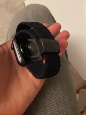 Apple Watch med svart flätat band - Snygg Apple Watch med svart flätat nylonband och rundad fyrkantig urtavla i svart aluminium. Klockan har en modern design och passar perfekt för dig som vill ha koll på både träning och notiser direkt på handleden. Jag har tyvärr inte laddare 