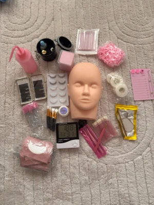 Kit för övning och tillbehör till fransar - Ett komplett kit med verktyg och tillbehör för fransar och bryn. Innehåller övningshuvud i silikon, rosa pumpflaska, borstar, pincetter, pads, limringar, rosa scrunchie, penslar, fransbrickor, tejp, termometer och förvaringsboxar. Flera delar i rosa och vitt.