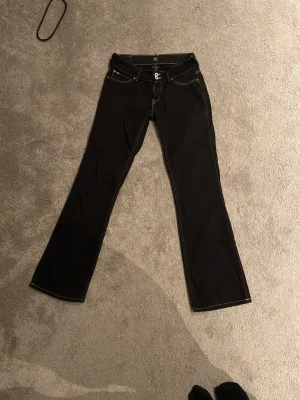 Svarta bootcut jeans från Lee - Säljer ett par svarta bootcut jeans från Lee med vita kontrastsömmar och dubbla knappar i midjan. Snygg passform men kommer tyvärr inte till användning. Inga defekter!💕Storlek:står ej men skulle säga Xs/S. Midjemått tvärsöver:35cm. Innerbenslängden 78cm