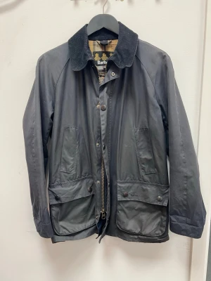 Barbour Ashby Jacka  - Vaxad jacka från Barbour i storlek S. Använd sparsamt och i mycket gott skick – inga synliga slitage eller defekter. Klassisk modell med tidlös design och slitstarkt material. Perfekt som allroundjacka för vardag och utomhusbruk. Redo att användas direkt.