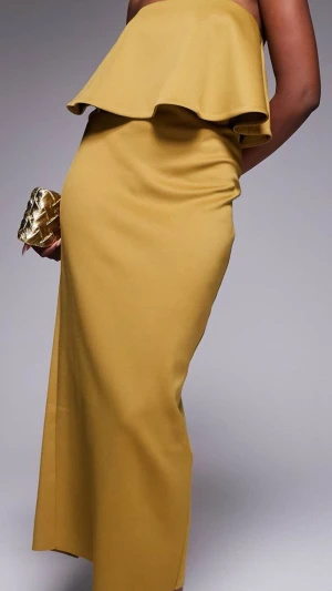 Bronze/olivegrön axelbandslös långklänning - Trendig bronze axelbandslös långklänning med volang upptill och slits baktill. Klänningen har en smickrande, figurnära passform och är perfekt för dig som vill sticka ut. Tillverkad i ett mjukt och följsamt material som ger en lyxig känsla. Helt ny och etiketten sitter kvar, nytt pris 600kr säljer för 250kr. Den är mer bronze och olivgrön i verkligheten. Super snygg.