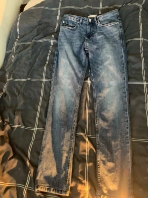 Blå slim jeans från Tom Tailor - Snygga blå jeans från Tom Tailor i modellen Regular Slim. Jeansen har en klassisk femficksdesign, knappgylf och slitna detaljer för en trendig look. Perfekta till sneakers och hoodie för en avslappnad stil.