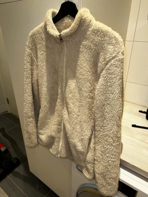Beige teddykofta från Uniqlo - Mysig teddykofta från Uniqlo i beige färg med dragkedja framtill och hög krage. Koftan är i storlek M men passar också L. Koftan är tillverkad i fluffigt, mjukt material som ger en avslappnad och trendig look. Perfekt för kyliga dagar när du vill vara både varm och snygg. Skriv över det minsta lilla eller över den minsta funderingen!🔥🔥