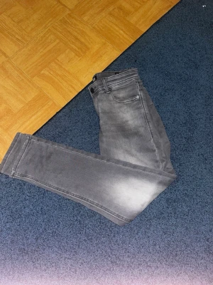 Grå slim fit jeans från Jack & Jones - Snygga grå slim fit jeans från Jack & Jones med klassisk femficksdesign och lätt slitna detaljer på låren. Jeansen har normal midja och smal passform hela vägen ner. Perfekta för en trendig och avslappnad stil.