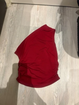 Röd oneshoulder topp  - Snygg röd oneshoulder topp i mjukt material. Toppen har en tight passform och cool asymmetrisk axel, perfekt för att sticka ut. Materialet känns stretchigt och bekvämt, och den har lätt rynkade detaljer på sidan.
