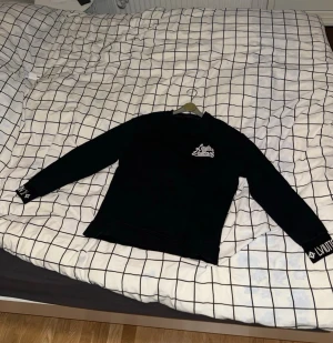 Svart Louis Vuitton sweatshirt - Svart sweatshirt från Louis Vuitton med vit broderad logga på bröstet och tryck på ärmsluten. Tröjan har rund halsringning och långa ärmar. Perfekt för dig som gillar streetwear och exklusiva märken.