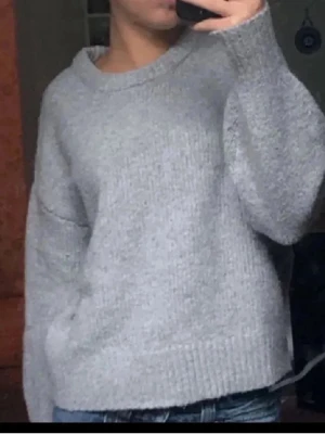 Ljusgrå oversized stickad tröja - Mysig ljusgrå stickad tröja med avslappnad passform och bred ribbad kant vid ärmslut och nederkant. Tröjan har rund halsringning och är perfekt för lager-på-lager-stil. Passar dig som gillar en enkel och stilren look. Små defekter som rödrosa fläckar vid halsringningen pga färg men ej super synligt 